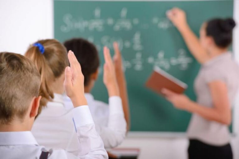 Niños en un salón de clases levantan la mano